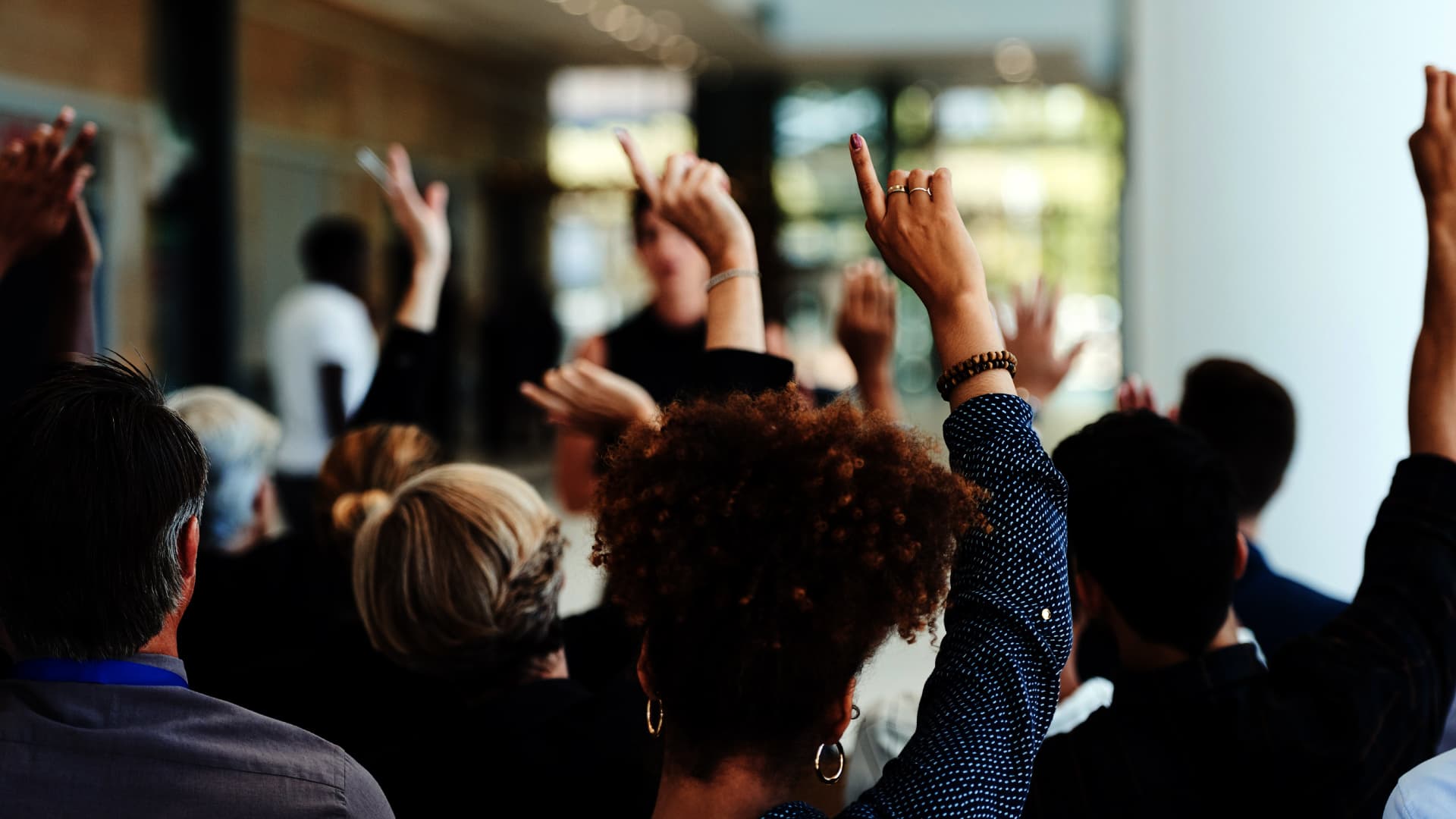 A group of professionals engaging with a speaker and raising their hands.