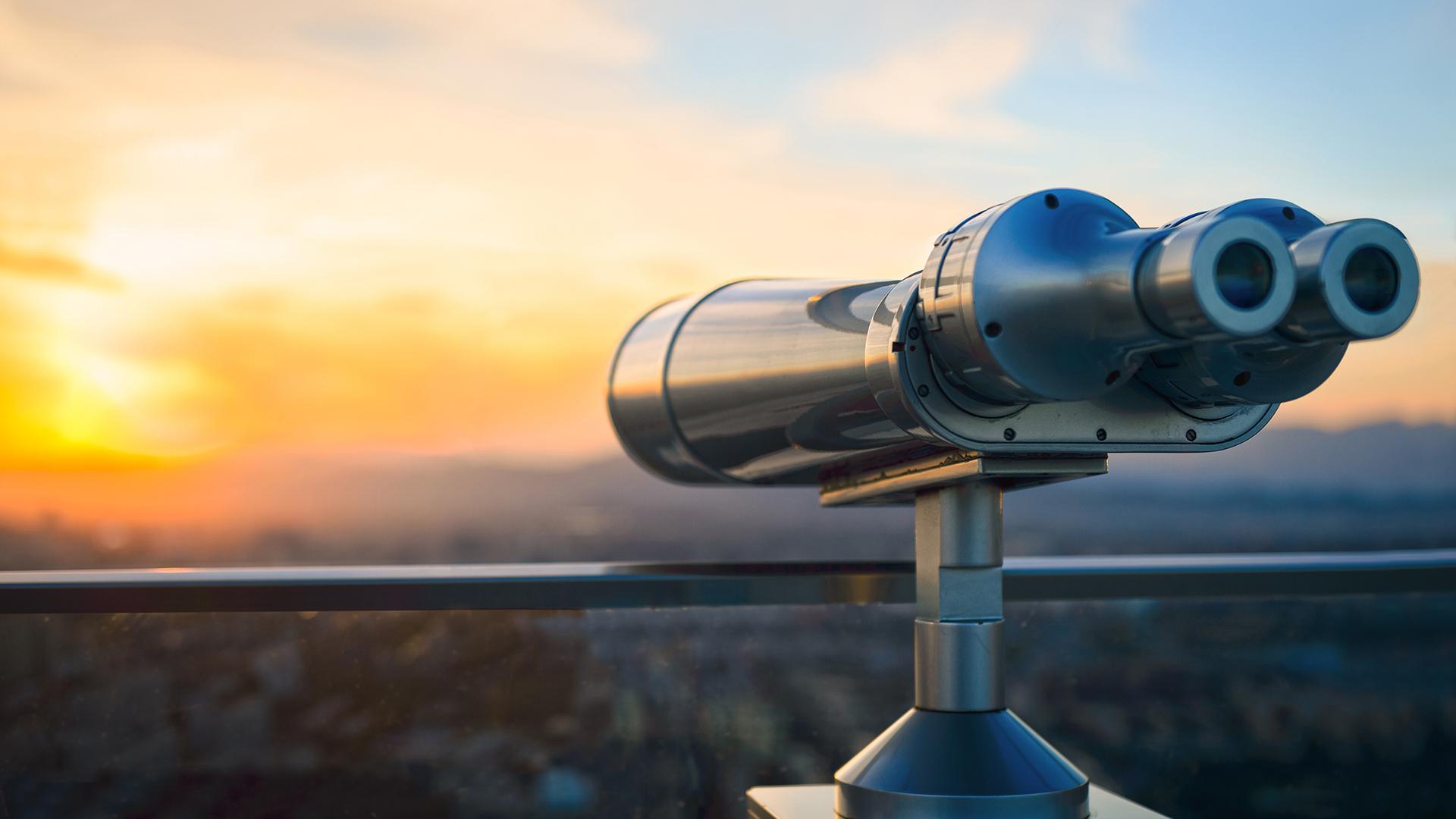 Coin-operated binoculars overlooking a sunset landscape.