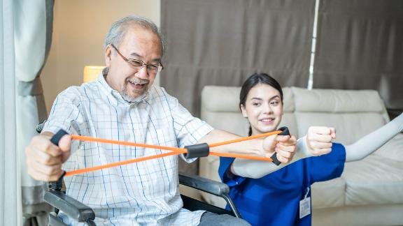 Elderly man in a wheelchair doing physiotherapist with support from therapist nurse