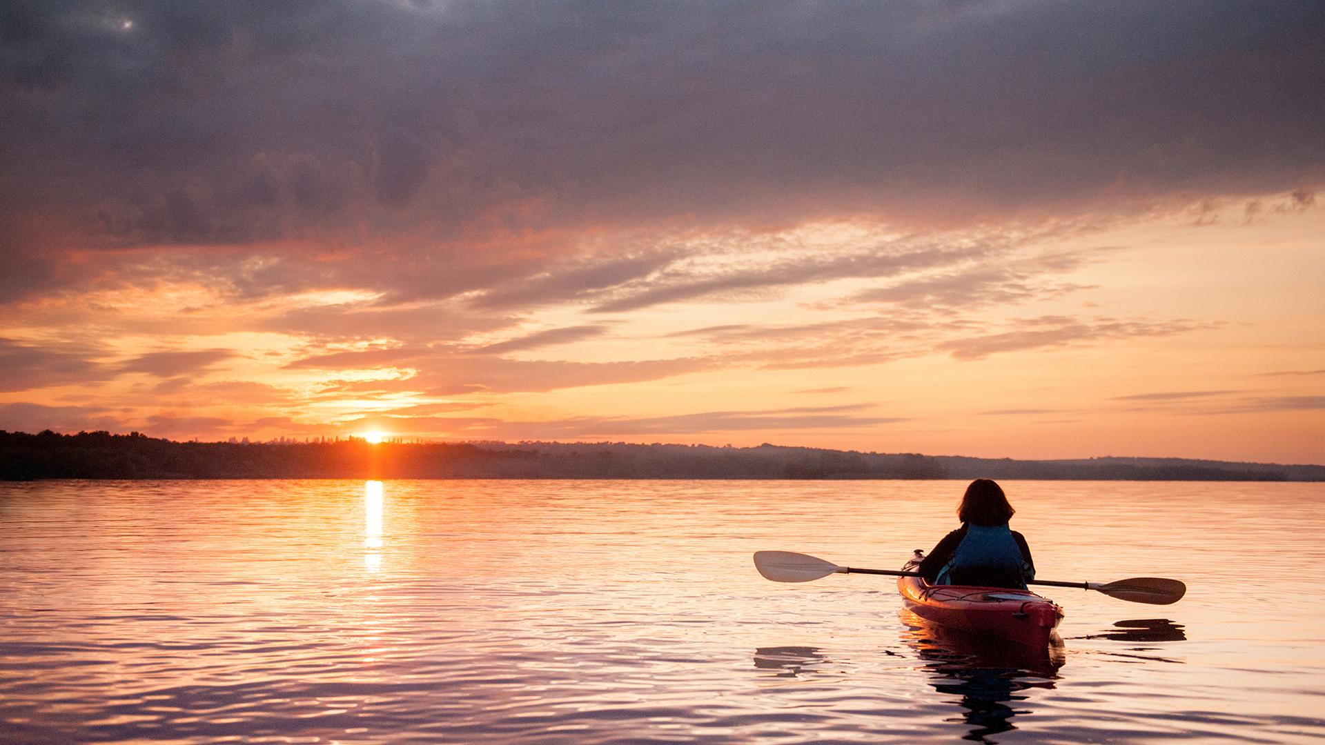 A person relaxing in a kayak while admiring a setting sun.