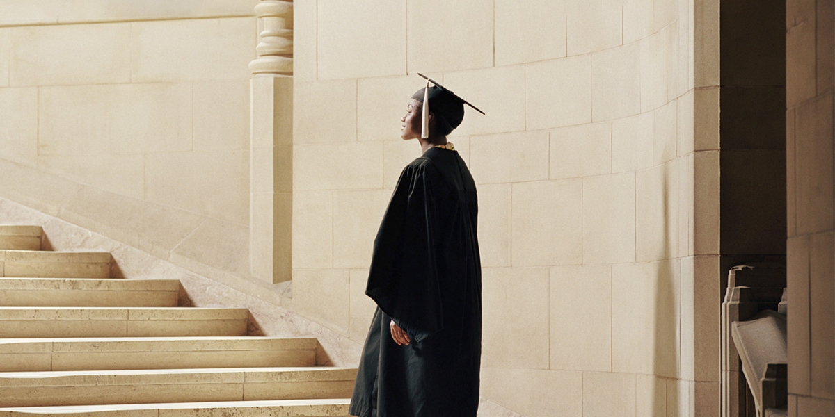 Women wearing graduation cap and gown, ascending staircase, rear view