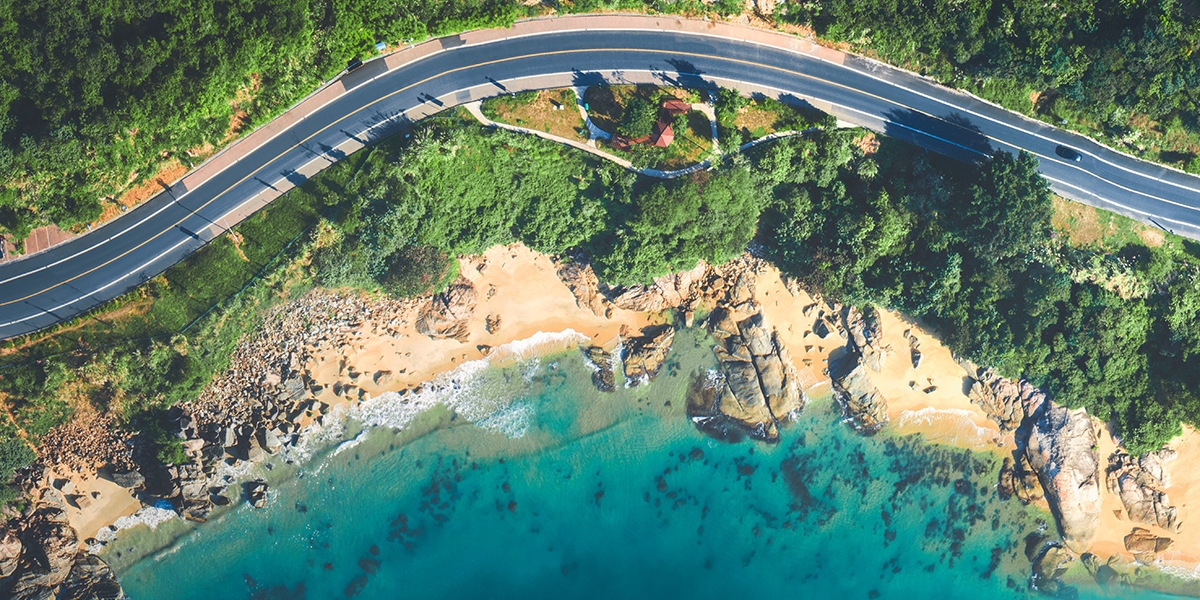 Birds eye view of a curved portion of road running along a beach front