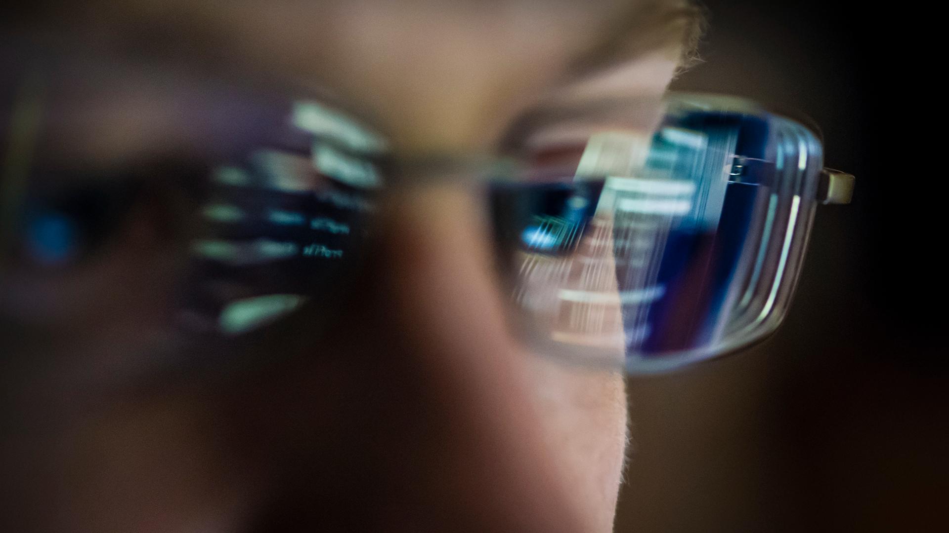 Close-up of a young programmer working on a computer with computer code reflecting in the man's glasses.