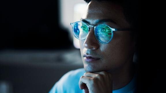  Asian man with computer code reflected in glasses.