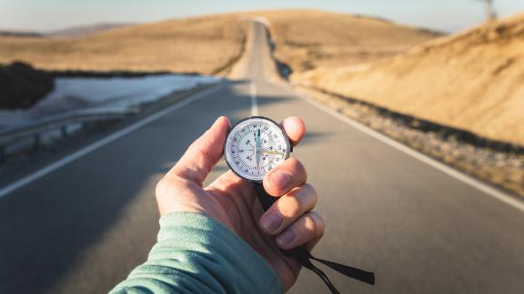 Person standing in the middle of a desert road holding a compass.