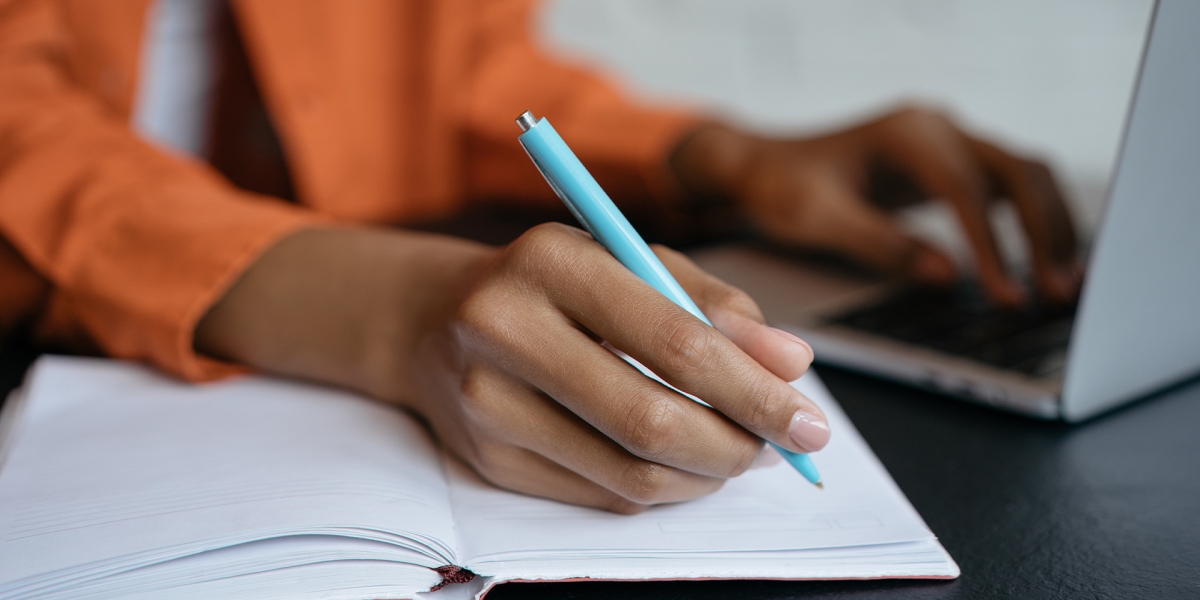 A close up of a woman's hands taking notes at a desk.