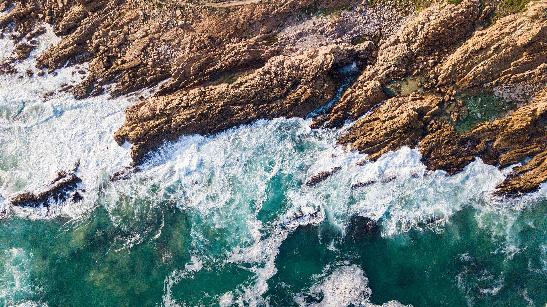 Aerial view of waves crashing along a rocky shoreline.