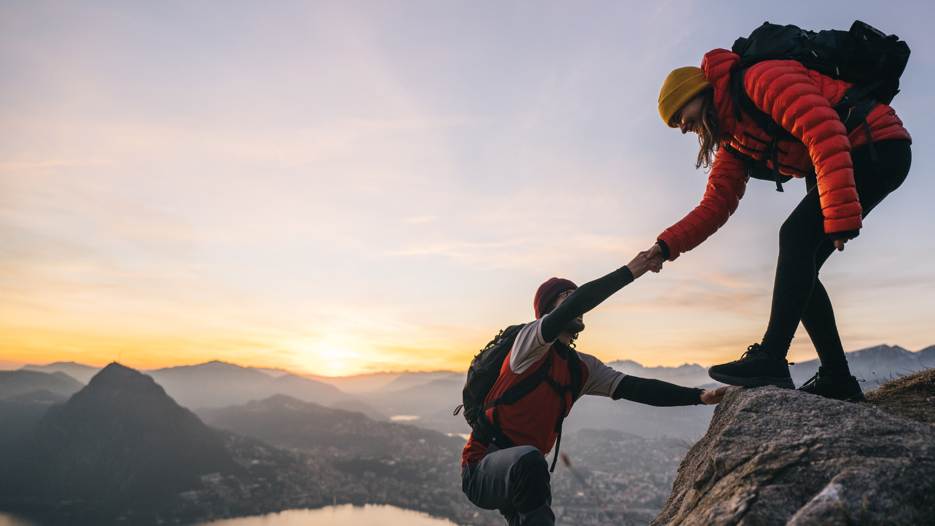 Two hikers helping each other up a mountain cliff.