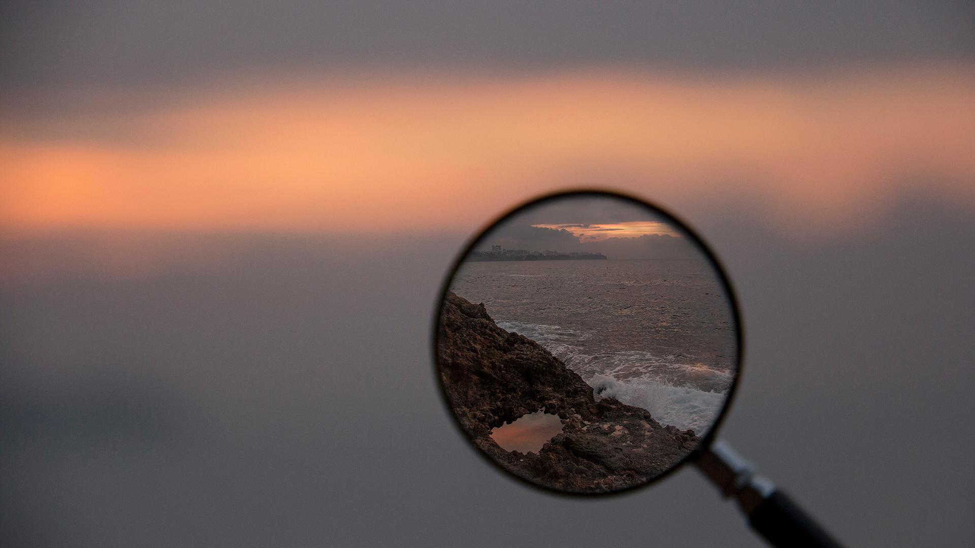 Person holding a magnifying glass that's focused on an ocean view.