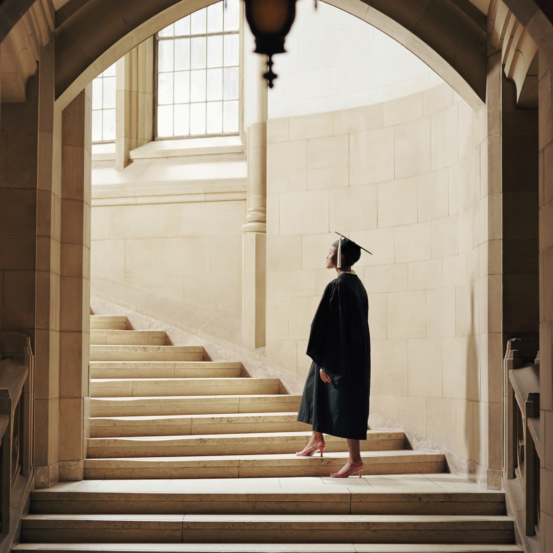 Woman in graduation cap and gown walking up stairwell