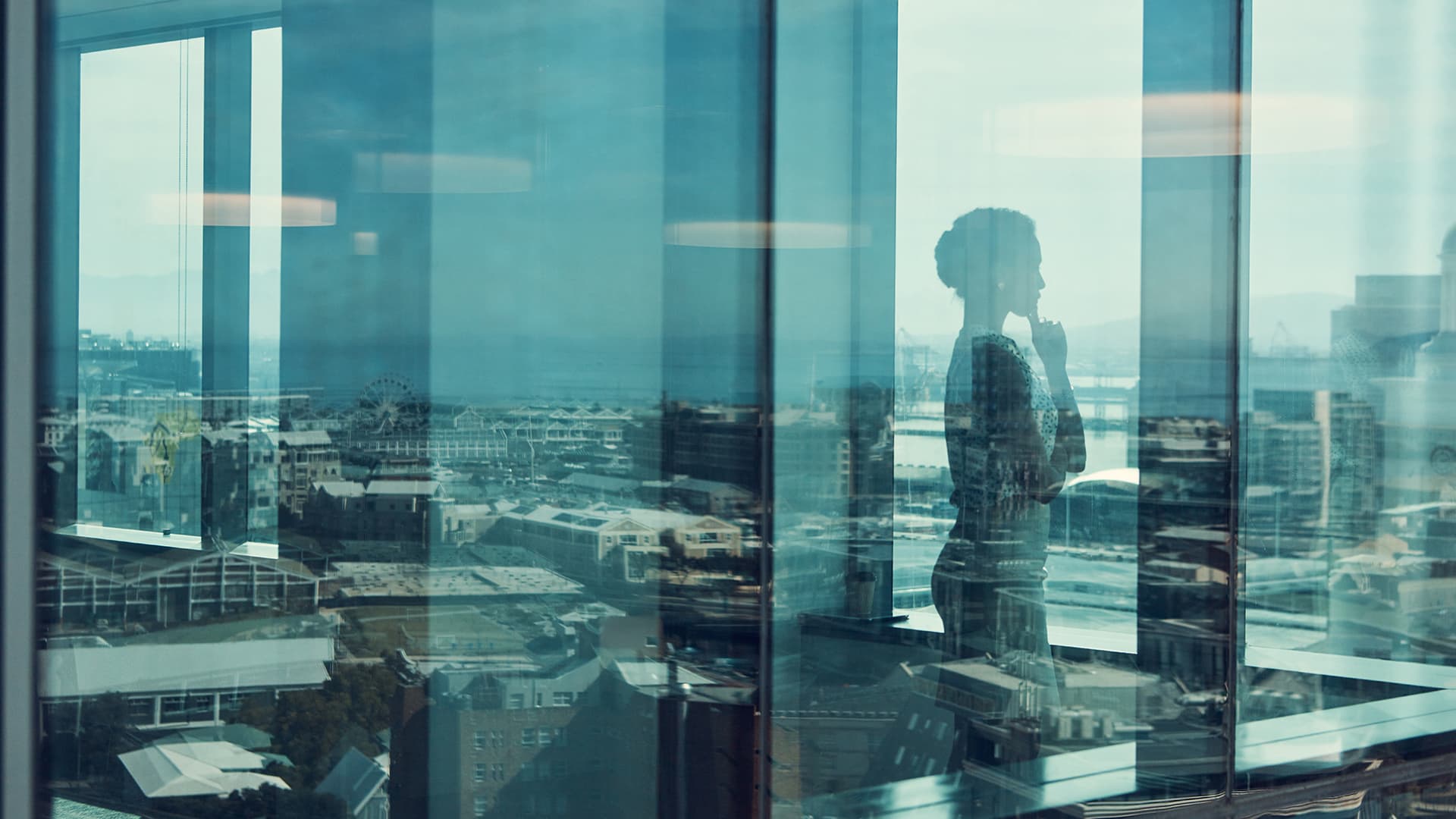 Businesswoman standing inside a glass building with a reflection of the city in the background.