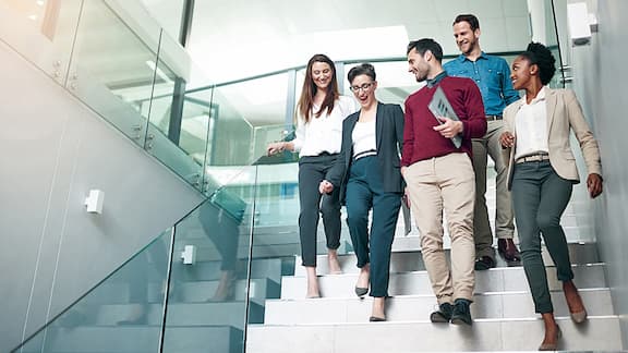 A group of colleagues talking together while walking down stairs in a large modern office