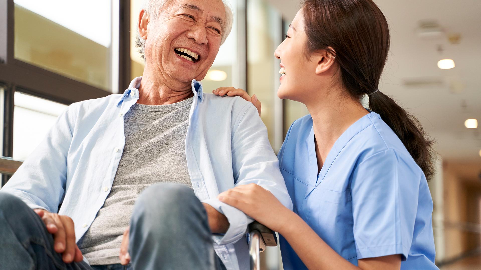 Friendly asian caretaker talking to senior patient in nursing home