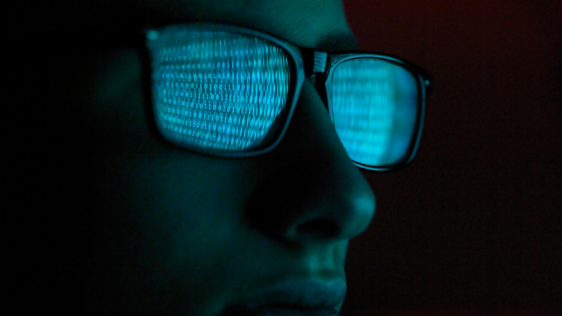 Binary code reflected in a hacker's glasses.