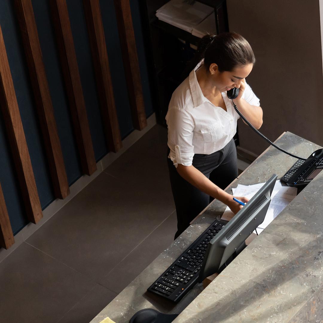 A secretary speaking on the phone at a reception desk.